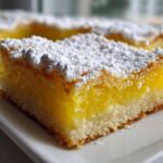 A close-up shot of one of the tantalizing lemon bars, featuring a thick, bright yellow filling and a shortbread crust, dusted heavily with powdered sugar.
