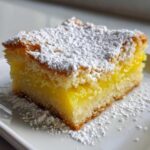 Close-up of a single, thick square of Tantalizing Lemon Bars, featuring a bright yellow filling and dusted heavily with powdered sugar.