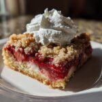 A single serving of Tasty Strawberry Shortcake Streusel Bars topped with a dollop of whipped cream on a white plate.
