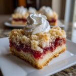 A close-up of a Tasty Strawberry Shortcake Streusel Bars square topped with a dollop of whipped cream.