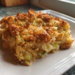 A close-up of a golden-brown serving of Zucchini and Yellow Squash Casserole on a white plate.
