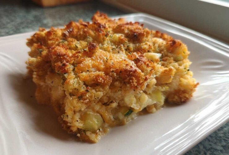 A close-up of a golden-brown serving of Zucchini and Yellow Squash Casserole on a white plate.