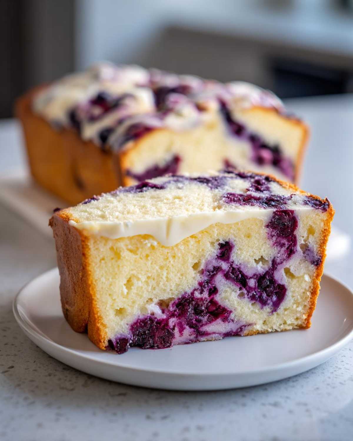 A thick slice of Blueberry Cream Cheese Bread Loaf with a white cream cheese glaze, showing moist crumb and burst blueberries.