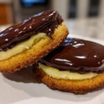 Close-up of two layered Boston Cream Pie Cookie Bites filled with vanilla cream and topped with shiny dark chocolate ganache.