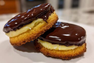 Close-up of two layered Boston Cream Pie Cookie Bites filled with vanilla cream and topped with shiny dark chocolate ganache.