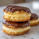 A close-up stack of two Boston Cream Pie Cookie Bites filled with vanilla cream and topped with rich chocolate ganache.