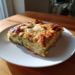 A square slice of Cheesy Zucchini Pizza Casserole with a bubbly, browned cheese topping, served on a white plate.