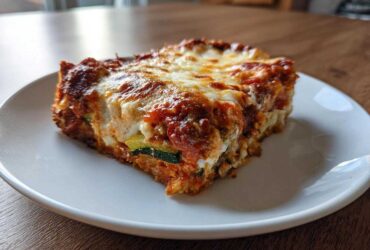 A thick slice of Cheesy Zucchini Pizza Casserole featuring layers of zucchini, sauce, and a bubbly, browned cheese topping.