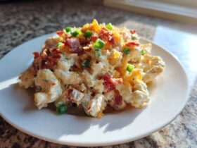 A serving of creamy Chicken Bacon Ranch Pasta Salad topped with crumbled bacon, shredded cheese, and green onions.
