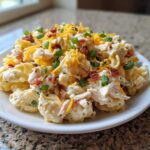 A generous serving of creamy Chicken Bacon Ranch Pasta Salad topped with shredded cheddar cheese, bacon bits, and green onions.