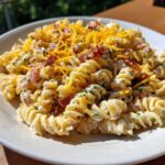 Close-up of creamy Bacon Pasta Salad made with rotini pasta, topped with bacon bits and shredded cheddar cheese.