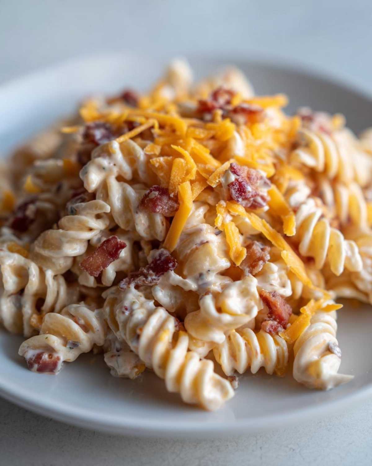 Close-up of creamy Bacon Pasta Salad made with rotini pasta, bacon bits, and topped with shredded cheddar cheese.