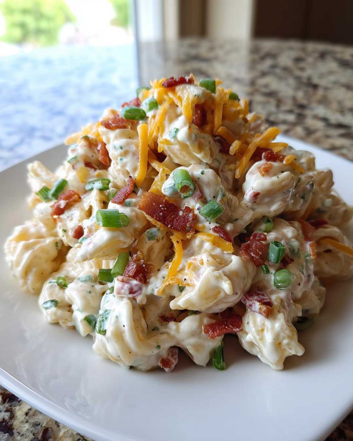 A close-up of a mound of creamy Chicken Bacon Ranch Pasta Salad topped with shredded cheese, bacon bits, and green onions.