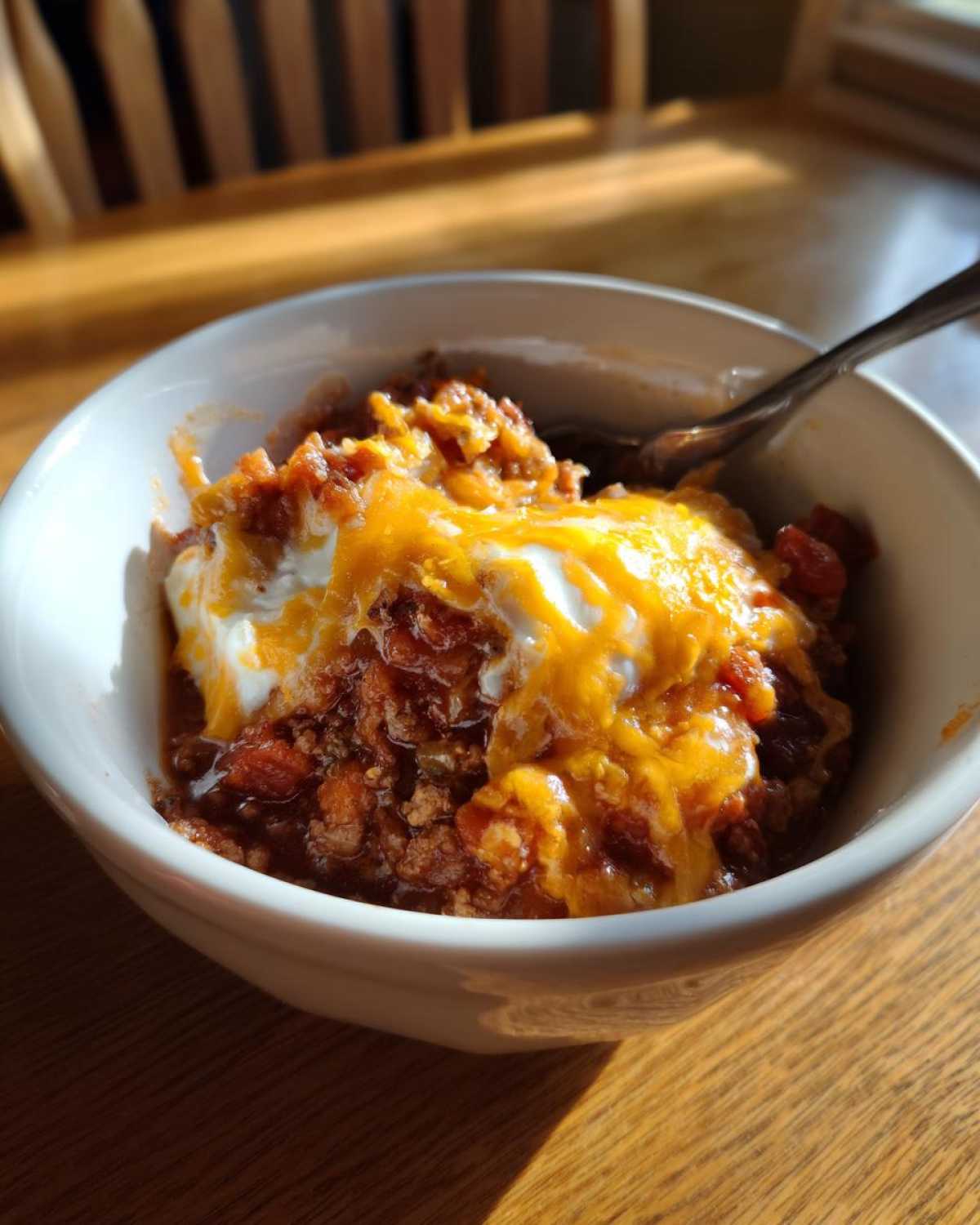 A close-up of a bowl of Crock Pot Cowboy Casserole topped with melted cheddar cheese and sour cream.