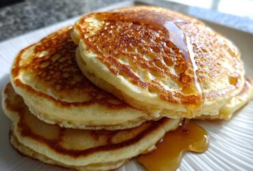 Close-up of a stack of three fluffy Buttermilk Pancakes drizzled generously with golden syrup.