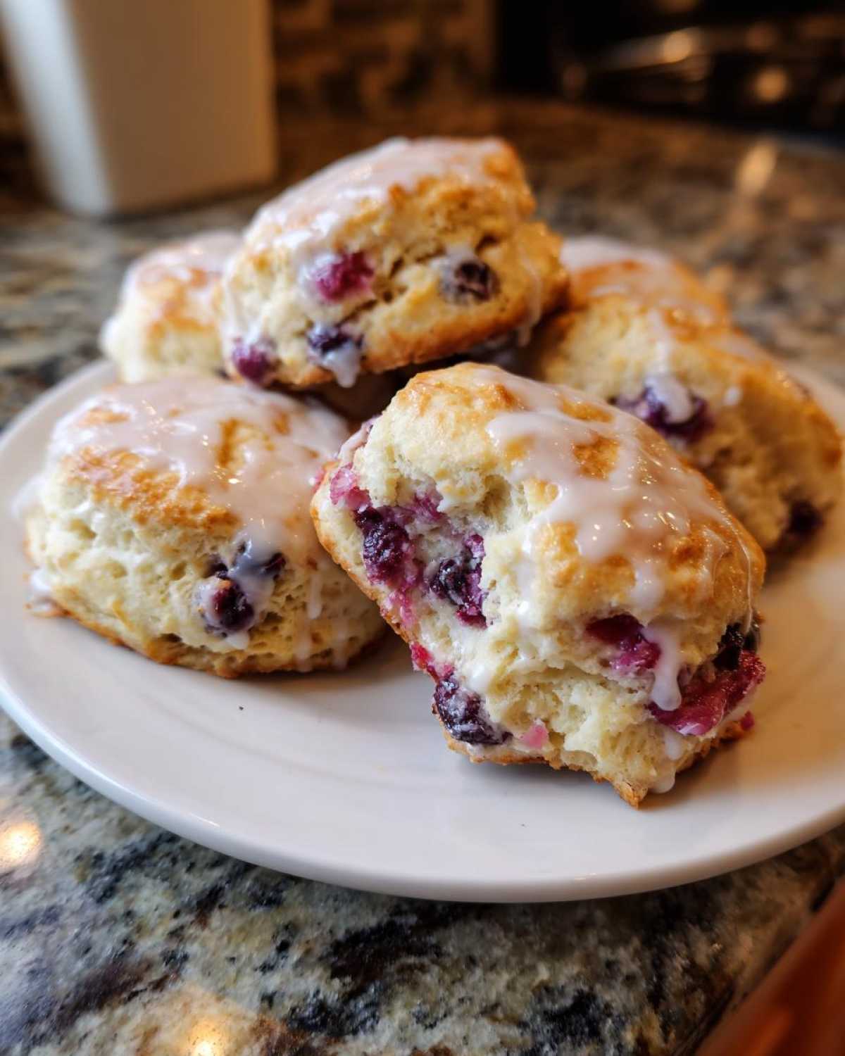 A stack of five freshly baked Blueberry Scones topped with a sweet white glaze, resting on a white plate.