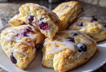 Close-up of several freshly baked, triangular Blueberry Scones drizzled with white glaze, showing a fluffy interior.