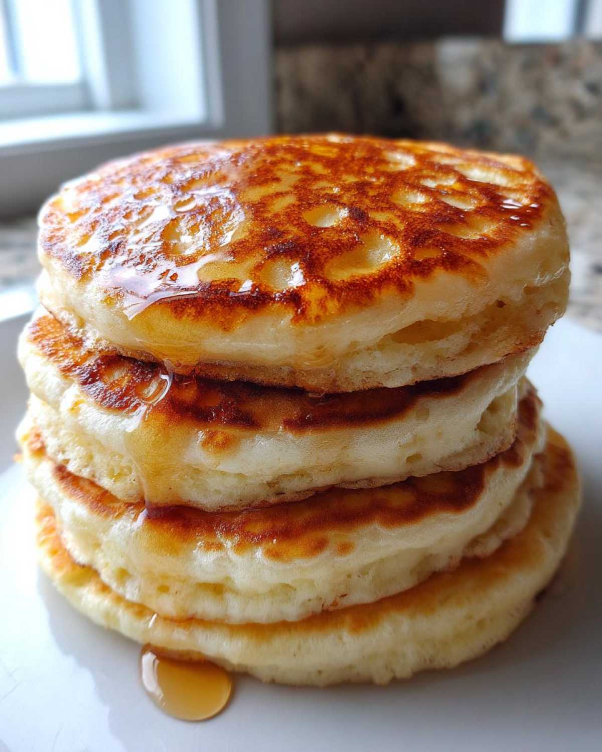 A tall stack of four fluffy Buttermilk Pancakes drizzled with golden syrup.