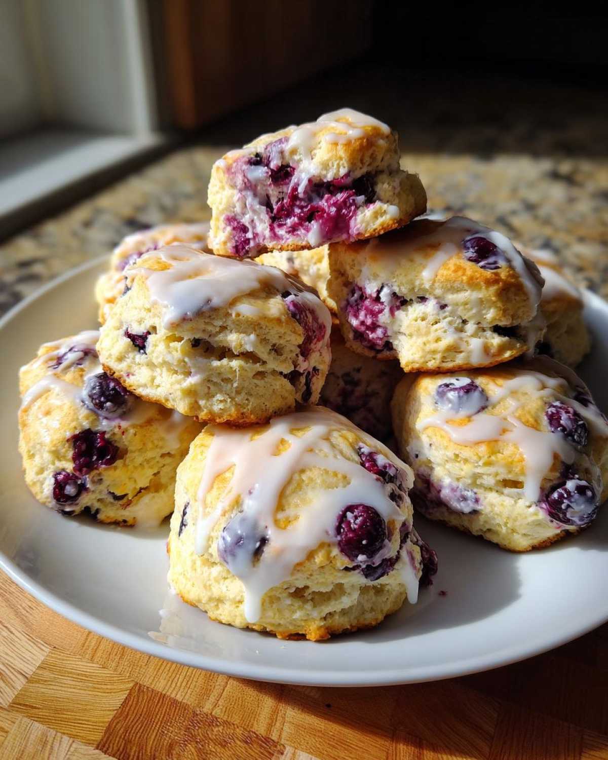 A stack of homemade Blueberry Scones drizzled with white glaze, showing the bright purple interior.