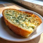 A golden-brown slice of homemade Garlic Bread with Garlic Powder, topped with melted butter and parsley, served on a white plate.