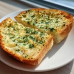 Two slices of golden brown Garlic Bread with Garlic Powder, topped with melted butter and fresh parsley, served on a white plate.
