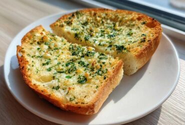 Two slices of golden brown Garlic Bread with Garlic Powder, topped with melted butter and fresh parsley, served on a white plate.