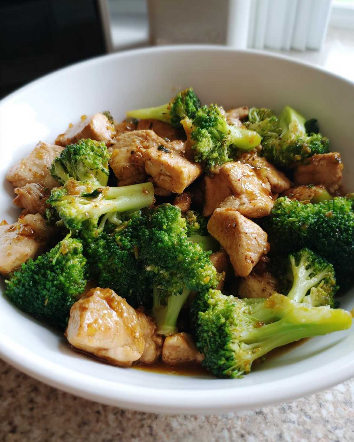 Close-up of Garlic Butter Chicken and Broccoli pieces coated in sauce, served in a white bowl.