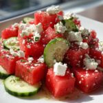 Close-up of bright red watermelon cubes topped with crumbled feta cheese and mint, mixed with cucumber slices in a Mediterranean Watermelon Salad.