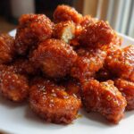 A close-up of crispy Orange Chicken Bites coated in a shiny, sticky orange glaze and sprinkled with sesame seeds.