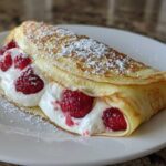 A single folded Raspberry Vanilla Crepes with Creamy Filling, topped with powdered sugar, served on a white plate.