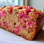 Close-up of a slice of homemade Rhubarb Bread showing moist crumb and bright pink rhubarb pieces throughout.