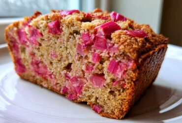 Close-up of a slice of homemade Rhubarb Bread showing moist crumb and bright pink rhubarb pieces throughout.