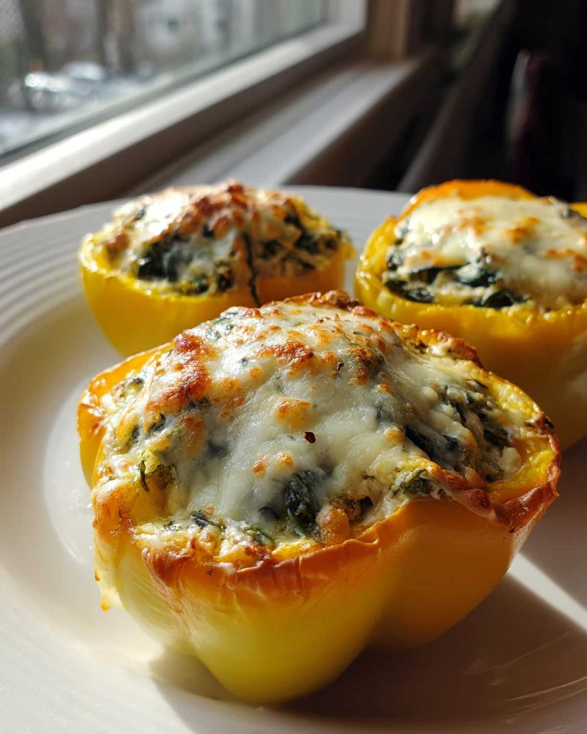Three baked yellow bell peppers filled with a creamy ricotta and spinach mixture, topped with browned, melted cheese, showcasing the Ricotta Stuffed Peppers.