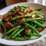 A close-up serving of bright green Sautéed Green Beans with Crispy Bacon piled high on a white plate.
