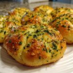 Close-up of several golden brown, soft Garlic Knots glistening with butter and topped with fresh chopped parsley.