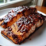 Two perfectly cooked fillets of Texas Roadhouse Style Baked Salmon covered in a thick, dark, savory glaze.