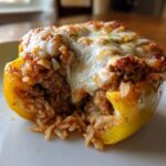 A close-up view of a single yellow stuffed bell peppers half, revealing a savory filling of ground meat and rice topped with melted cheese.