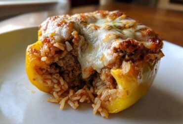 A close-up view of a single yellow stuffed bell peppers half, revealing a savory filling of ground meat and rice topped with melted cheese.