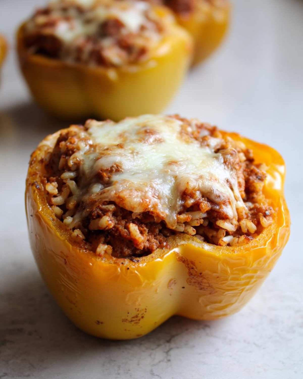 A close-up shot of a baked yellow stuffed bell peppers, filled with meat and rice mixture and topped with melted cheese.